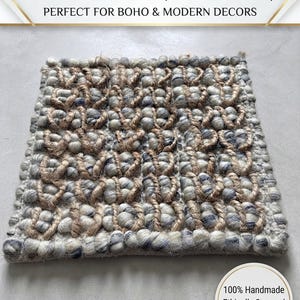 Könnte beinhalten: Ein quadratischer, handgewebter Teppich mit einem strukturierten Muster aus grauen und weißen Wollnoppen, durchsetzt mit natürlichen, hellbraunen Jutefasern. Der Text auf dem Bild lautet: AUTHENTIC HANDWOVEN BOBBLE RUG, Textured Wool & Natural Jute, Artisan Craftsmanship, PERFECT FOR BOHO & MODERN DECORS, 100% Handmade, Ethically Sourced, Limited Edition.