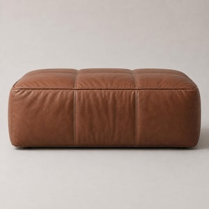 May include: A rectangular ottoman upholstered in smooth, medium-brown leather. The surface features a grid of stitched seams creating six distinct, padded rectangular sections across the top and front faces, with a low-profile, block-like shape.