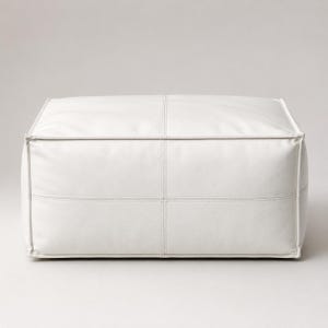Peut inclure: Un pouf rectangulaire blanc à la finition mate et lisse. L'objet présente des lignes structurées et nettes avec des coutures apparentes formant un motif en grille sur les surfaces avant et supérieure, créant un aspect géométrique uniforme.