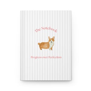 Könnte beinhalten: Ein weißes Notizbuch mit dünnen vertikalen grauen Streifen und einer Aquarellillustration eines braun-weißen Corgis in der Mitte. Der Text "The Notebook" ist in Pink über dem Hund und "Progress over Perfection" darunter gedruckt.