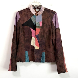 May include: A brown jacket featuring a dark floral pattern and a multi-colored patchwork design along the front opening. The garment includes a stand-up collar, long sleeves with lavender accents, and two vertical teal panels at the lower hem.