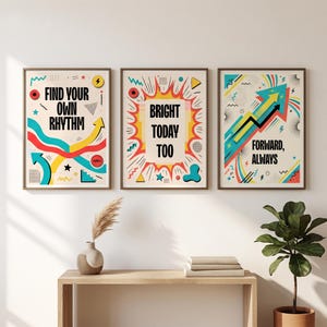Peut inclure: Un ensemble de trois affiches murales rectangulaires aux motifs graphiques colorés. La première affiche indique FIND YOUR OWN RHYTHM, la deuxième BRIGHT TODAY TOO, et la troisième FORWARD, ALWAYS. Chaque affiche comporte des flèches, des étoiles et des formes géométriques.