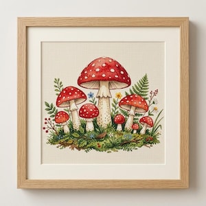 May include: A cross-stitch embroidery of a cluster of red and white spotted mushrooms surrounded by green ferns and small wildflowers, presented in a light-colored wooden frame with a cream-colored mat board border.