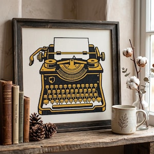 May include: A framed cross-stitch embroidery featuring a black and yellow typewriter design on a white fabric background. The typewriter is depicted with a blank sheet of paper inserted, detailed keys, and a carriage return lever, all set in a dark wood frame.