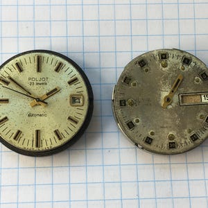 Könnte beinhalten: Zwei kreisförmige Uhrwerke. Das linke Uhrwerk hat ein cremefarbenes Zifferblatt mit goldfarbenen Zeigern, Indizes, einem Datumsfenster und dem Text POLJOT 23 jewels automatic. Das rechte Uhrwerk hat ein verwittertes silbernes Zifferblatt.