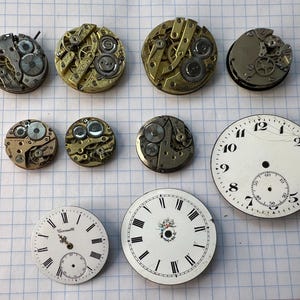 Puede incluir: Una colección de diez componentes de relojes antiguos, que incluye siete movimientos mecánicos circulares en tonos latón y plata, y tres esferas blancas con números romanos y arábigos negros y detalles florales decorativos.