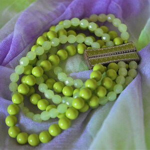 May include: A multi-strand bracelet featuring alternating rows of opaque lime green beads and translucent pale yellow faceted beads. The strands are secured by a rectangular, metallic gold-toned magnetic clasp with a textured, dotted pattern.