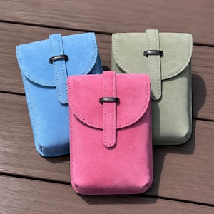 May include: Three rectangular pouches with a soft matte texture, each featuring a rounded flap closure secured by a vertical strap and a dark metal buckle. The pouches are coloured in bright blue, vibrant pink, and muted sage green respectively.