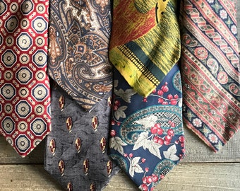 May include: Five patterned neckties in various designs and colors are displayed against a weathered wood background. The ties feature paisley, floral, and geometric patterns in shades of red, blue, green, and brown. The ties are folded and arranged vertically.