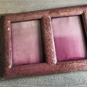 May include: A vintage double photo frame with a burgundy finish and ornate gold floral detailing. The frame has two openings and is made of a sturdy material. The frame is designed to hold two photos.