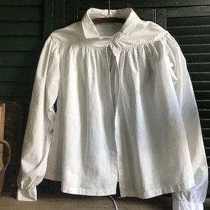 May include: A white, long-sleeved shirt with a gathered neckline and a tie closure. The shirt is made of a lightweight fabric and has a relaxed fit.