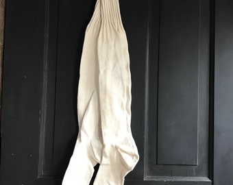 May include: A pair of white knee-high socks hanging on a hook against a black wooden background.