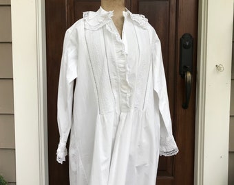 May include: A white cotton nightgown with lace trim and a ruffled collar. The gown has a long sleeve and a gathered skirt.