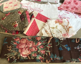 May include: Assortment of vintage fabric scraps in various patterns and colors. Includes floral prints, geometric designs, and patchwork pieces. The color palette features pinks, reds, browns, and creams, with some pieces showing signs of wear.