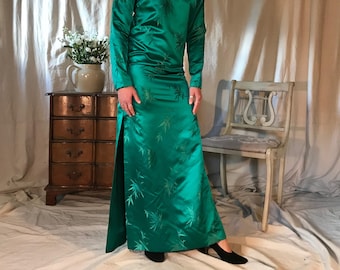 May include: A long, emerald green satin dress with a high neck and a side slit. The dress features a subtle bamboo print.