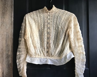 May include: A vintage cream-coloured lace blouse with a high neck and long sleeves. The blouse has a button-up front and a delicate lace trim around the neckline and cuffs.