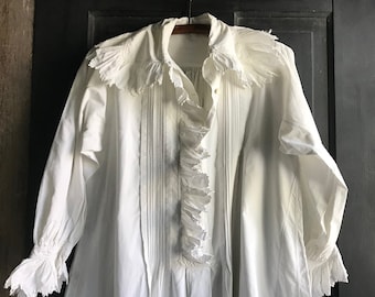 May include: A white cotton shirt with a ruffled collar and cuffs. The shirt has a gathered front and a long, flowing silhouette.