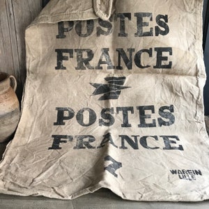Puede incluir: Un saco de correo de lona marrón vintage con el texto "POSTES FRANCE" impreso en negro. El saco tiene un aspecto desgastado y descolorido, lo que sugiere que se ha utilizado durante muchos años. El texto "WAREN LILLE" está impreso en letras más pequeñas en la parte inferior del saco.