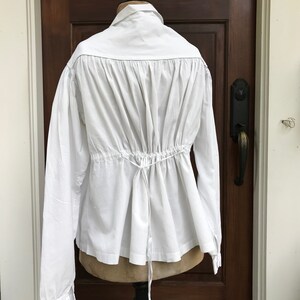 May include: A white long-sleeved shirt with a gathered back and a drawstring at the waist.