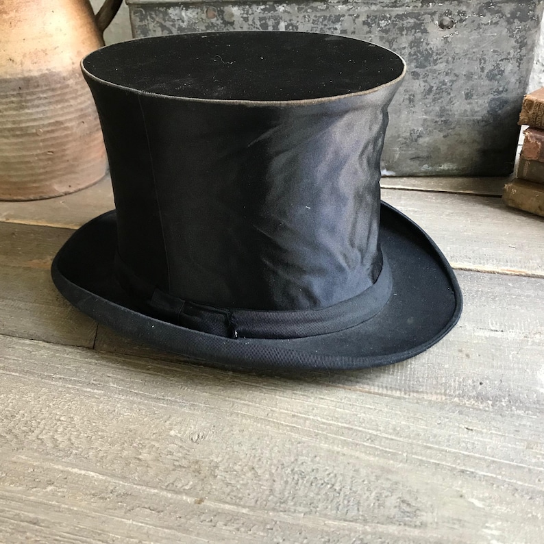 May include: A black top hat with a tall, cylindrical crown and a wide brim. The hat is made of a smooth, shiny material.