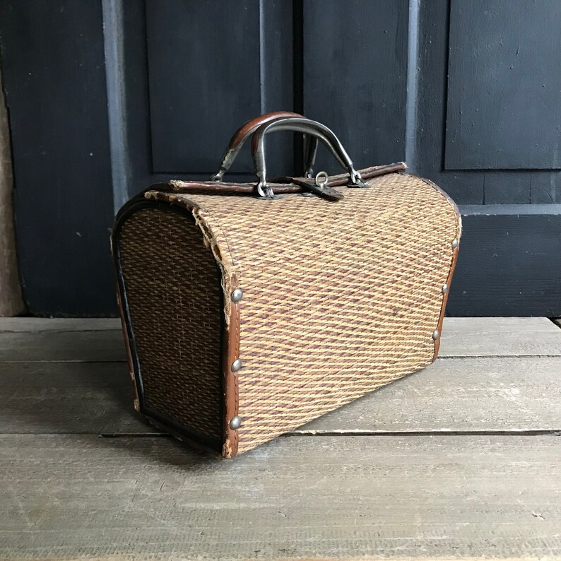 May include: A vintage woven wicker suitcase with a brown leather trim and a metal handle. The suitcase has a worn, antique look.