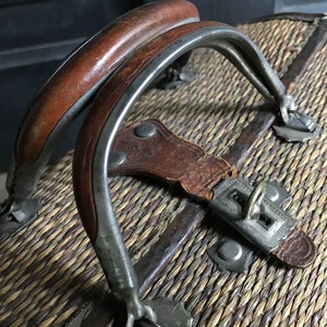 May include: A vintage wicker suitcase with a leather strap and metal clasps. The suitcase has a woven pattern and a brown leather handle.