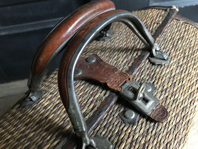 May include: A vintage wicker suitcase with a leather strap and metal clasps. The suitcase has a woven pattern and a brown leather handle.