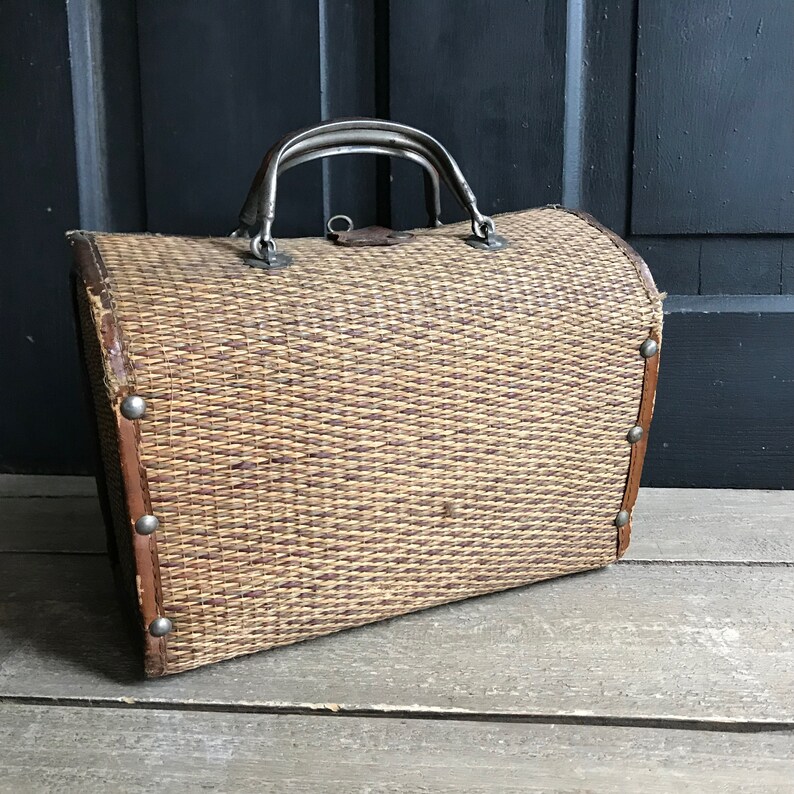 May include: A vintage woven wicker suitcase with a metal handle and decorative metal accents. The suitcase is brown and has a rectangular shape.