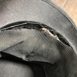 May include: Close-up of the inside of a black hat showing the stitching and lining. The lining is made of a black fabric with a ribbed texture.