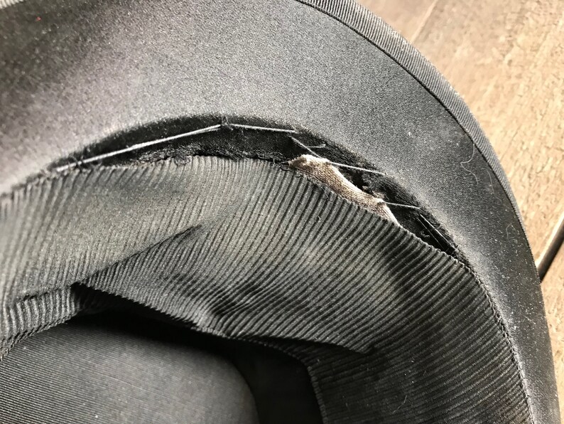 May include: Close-up of the inside of a black hat showing the stitching and lining. The lining is made of a black fabric with a ribbed texture.