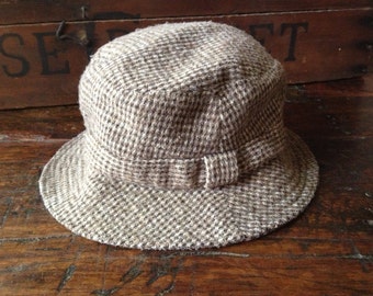 Könnte beinhalten: Ein brauner und weißer Tweed-Bucket-Hut mit einem braunen Band.