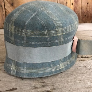 以下が含まれることがあります： 青と黄色の格子柄の帽子に、幅広のグレーのリボンとピンクのリボンがついた帽子です。