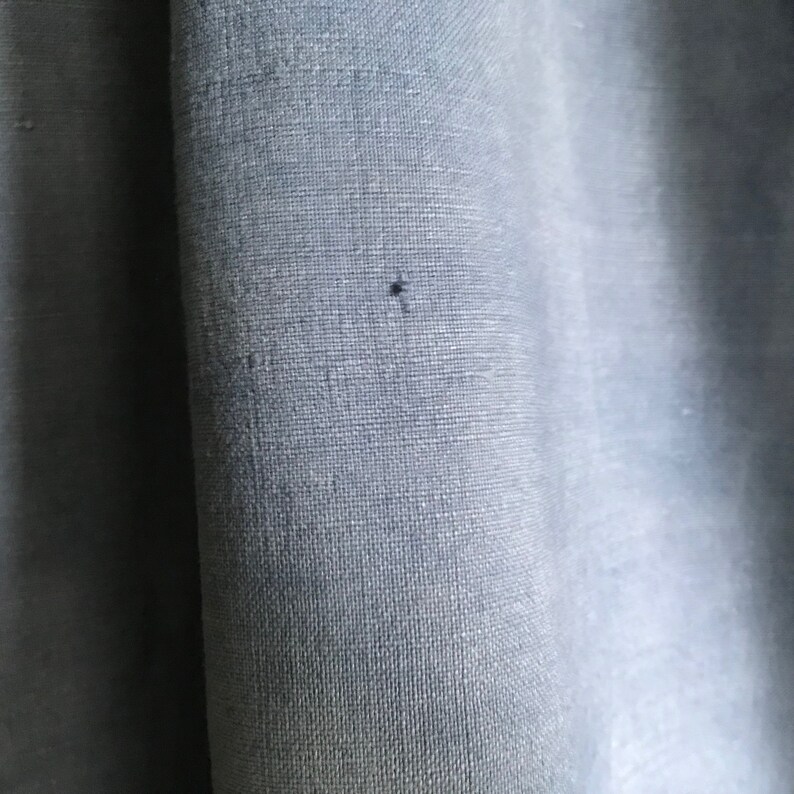 May include: Close-up of a light blue fabric with a subtle woven texture. The fabric has a small dark spot in the center.