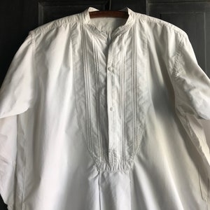 May include: A white long-sleeved shirt with a mandarin collar and a button-up front. The shirt has decorative stitching down the front.