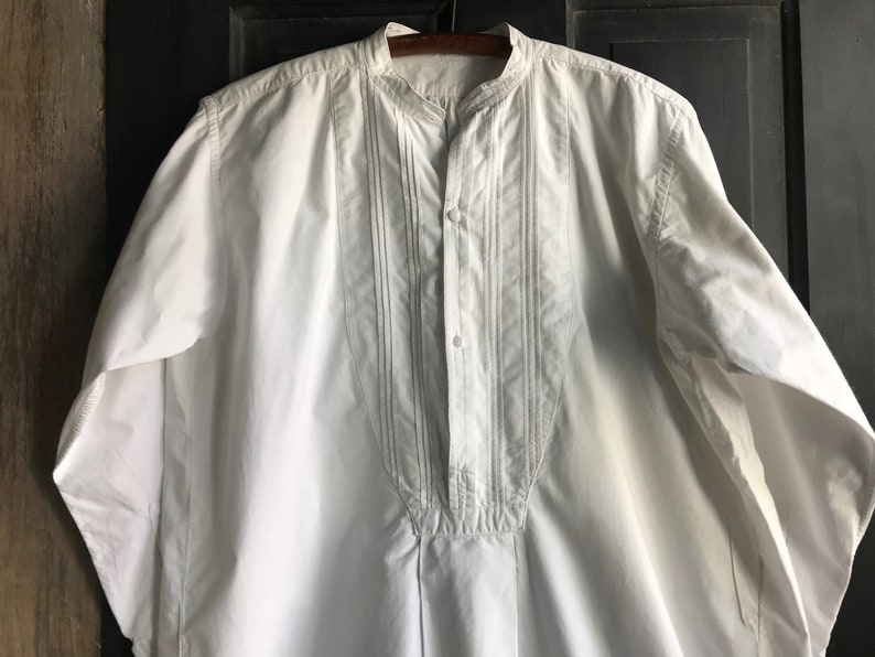 May include: A white long-sleeved shirt with a mandarin collar and a button-up front. The shirt has decorative stitching down the front.