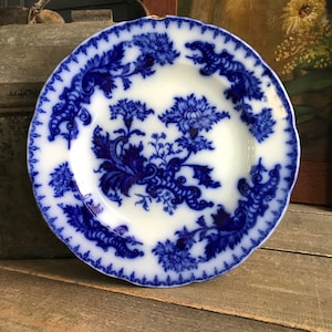 Puede incluir: Un plato de porcelana azul y blanco con un diseño floral. El plato tiene un borde festoneado y está decorado con flores y hojas azules.
