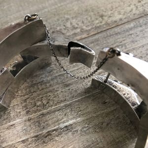 May include: A silver bracelet with a chain link closure. The bracelet is made of multiple interlocking pieces, creating a geometric design.