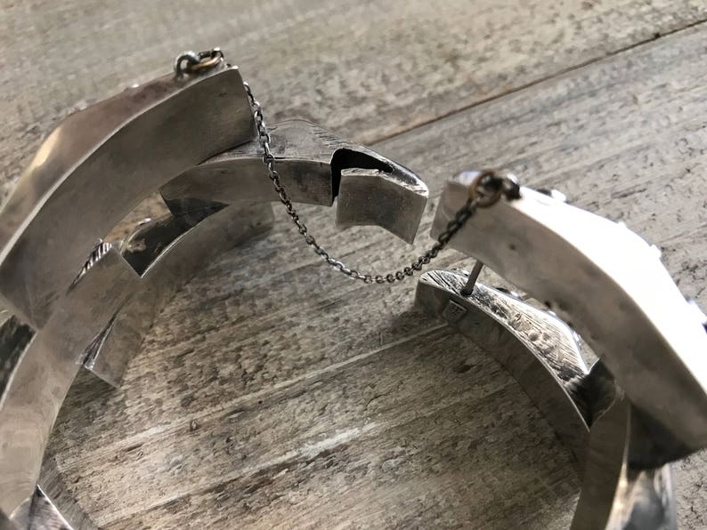 May include: A silver bracelet with a chain link closure. The bracelet is made of multiple interlocking pieces, creating a geometric design.