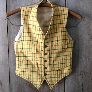 May include: A yellow, black, and red plaid vest with a button closure. The vest has two pockets on the front.