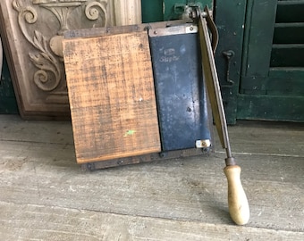 May include: Vintage paper cutter with a wooden base and a metal blade. The blade is labeled "Simplex".