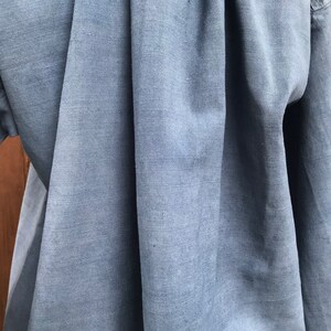 May include: Close-up of a blue linen fabric with a smooth, textured surface. The fabric is folded and draped, showcasing its soft and natural texture.