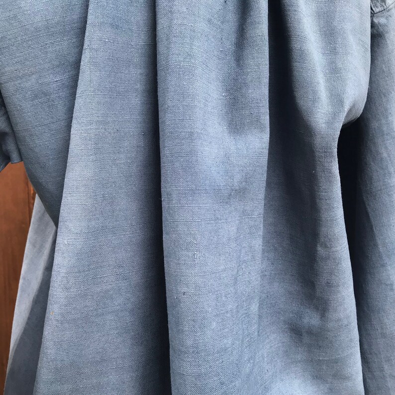 May include: Close-up of a blue linen fabric with a smooth, textured surface. The fabric is folded and draped, showcasing its soft and natural texture.