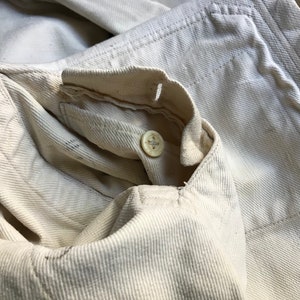 K&ouml;nnte beinhalten: Nahaufnahme eines cremefarbenen Jeansjackenkragens mit Knopfverschluss. Der Stoff hat ein strukturiertes Aussehen mit sichtbaren Nahtdetails. Der Knopf ist hellbeige.