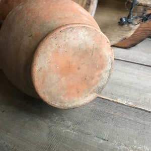 May include: A terracotta clay pot with a rounded bottom and a wide opening. The pot has a rough, textured surface and is a light brown color.