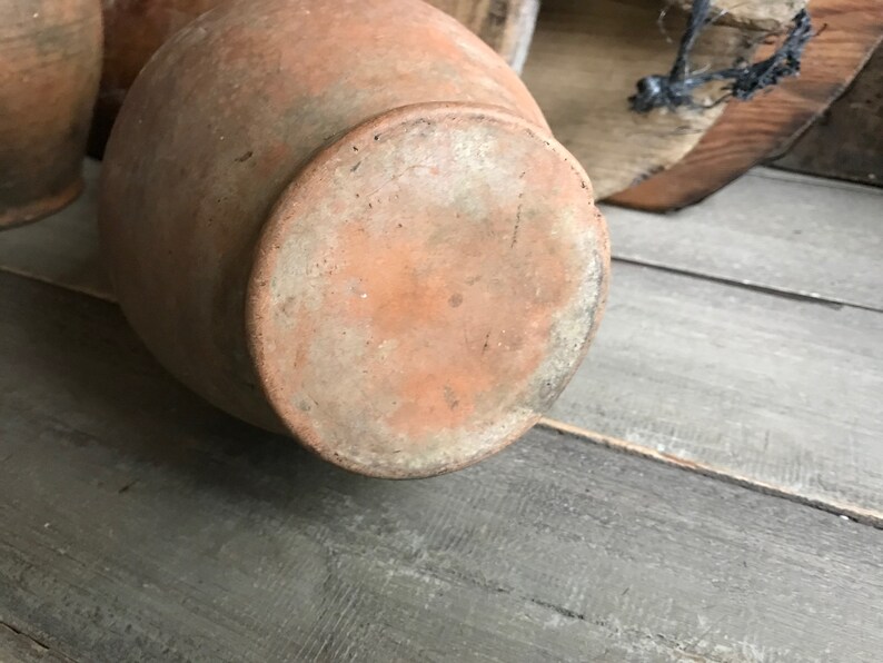 May include: A terracotta clay pot with a rounded bottom and a wide opening. The pot has a rough, textured surface and is a light brown color.