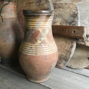 May include: Three brown clay jugs with yellow and white painted designs. The jugs are sitting on a wooden surface.