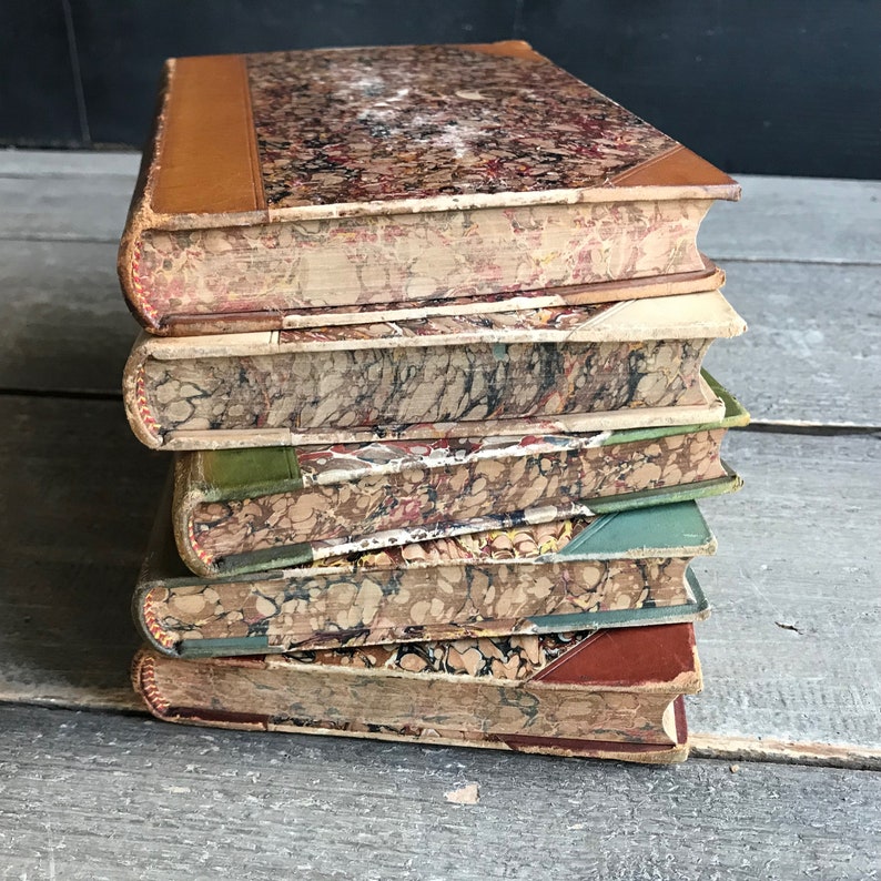 May include: A stack of six vintage hardcover books with marbled covers. The books are bound in leather and have a worn, antique look.