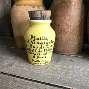 Puede incluir: Un pequeño tarro de cerámica amarillo con tapón de corcho. El tarro tiene texto manuscrito negro en francés. El texto incluye la palabra "Maille" y la fecha "27 août 1769". Un recipiente de condimentos vintage.