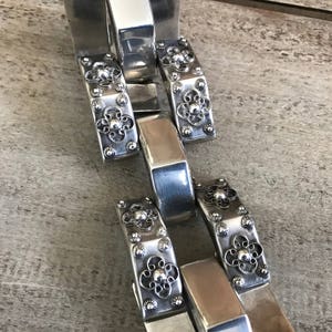 May include: Silver bracelet with a chain link design and decorative floral accents.