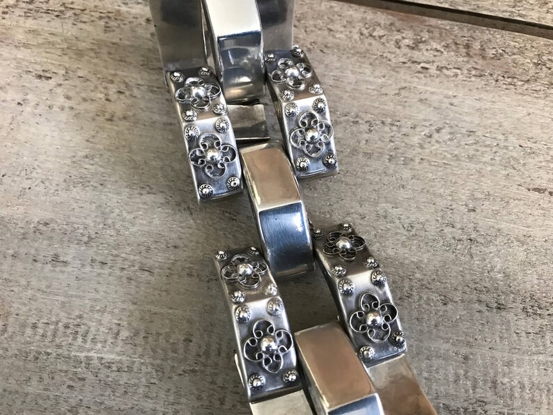 May include: Silver bracelet with a chain link design and decorative floral accents.